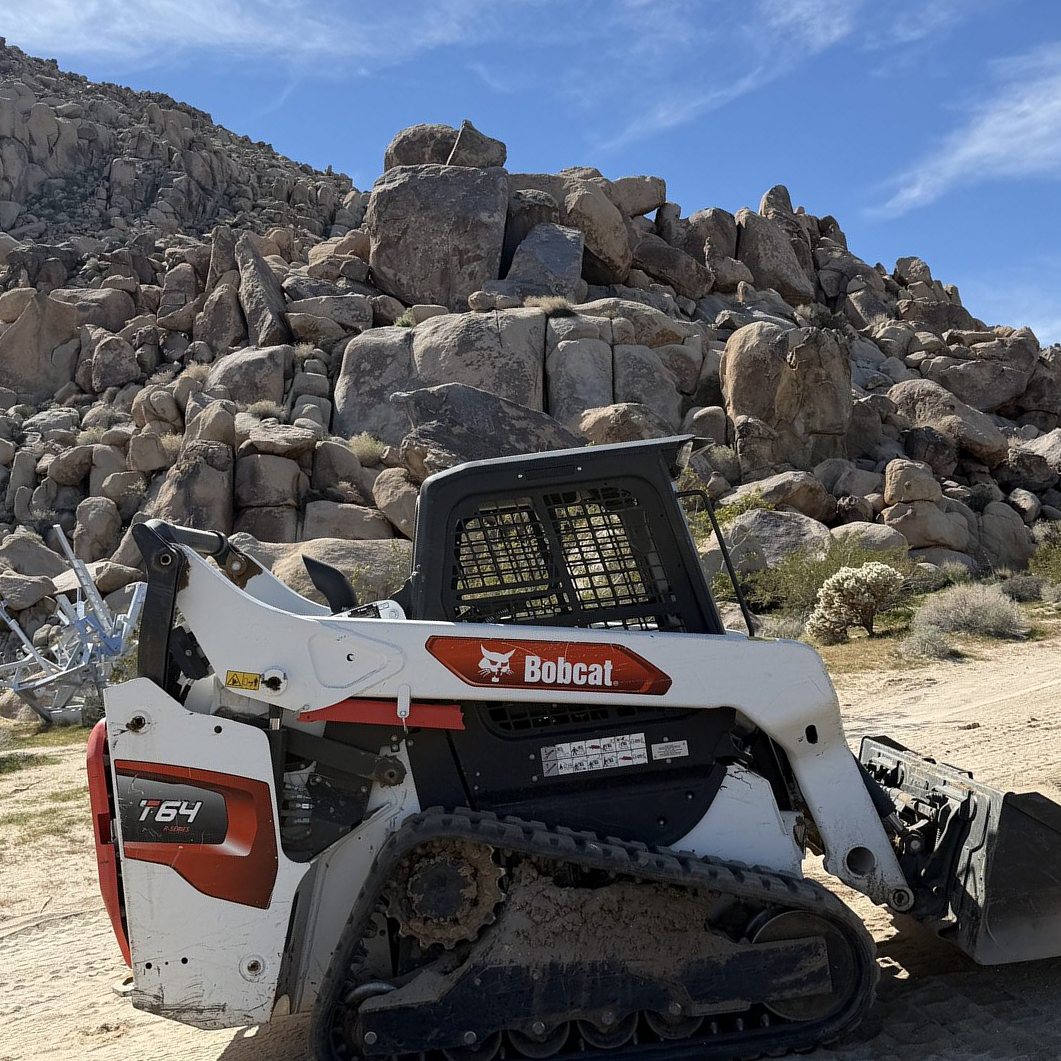 Bobcat T64 track loader on a graded pad below a granite boulder outcrop